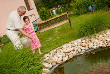 Grandparent-and-grandchild-standing-at-edge-of-fishpond